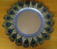 a mirror with peacock feathers on it sitting on a wooden floor next to a wall