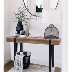 a table with a mirror and vase on top of it next to a black basket