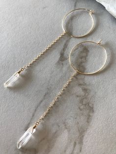 These delicate gold hoop earrings are simple yet unique. Dainty raw or polished crystal quartz gems are wrapped in wire and dangle from sparkly chain.Hoops are 2 inches in diameter, chain is 2.5 inches, and crystal quartz gemstone is anywhere from 0.75-1 inch long. Exact shape and size of natural quartz gems will vary slightly. Total earrings length will be about 5 inches long.You get to pick either raw or polished crystals. ~Reasons to love crystal quartz~Clear quartz amplifies energy and is us White Dangle Threader Earrings, Quartz Hoop Earrings, Crystal Quartz Earrings, Boho Wedding Earrings, Earrings Feather, Minimalist Earrings Gold, Turquoise Hoop Earrings, Long Gold Earrings, Big Hoop Earrings