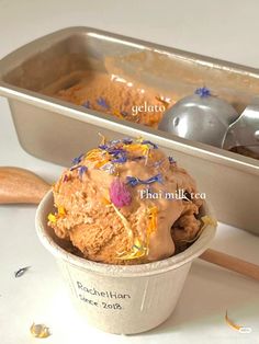 a scoop of ice cream in a paper cup next to a metal pan with spoons