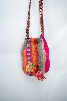 a multicolored purse hanging from a hook on a white wall with a chain attached to it