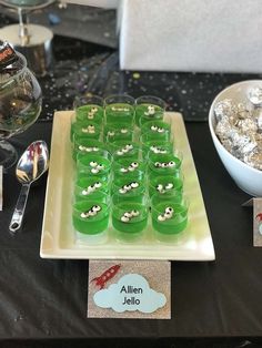 a table topped with lots of green cups filled with candy next to silver spoons