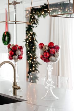 two glass goblets filled with christmas decorations on a counter top next to a wreath