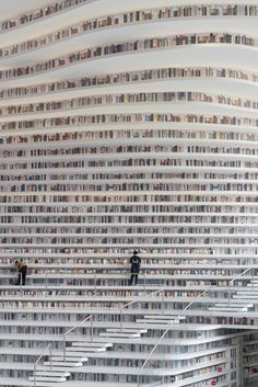 two people are standing on the stairs in front of a huge book shelf filled with books