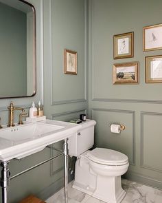 a white toilet sitting next to a sink in a bathroom under framed pictures on the wall