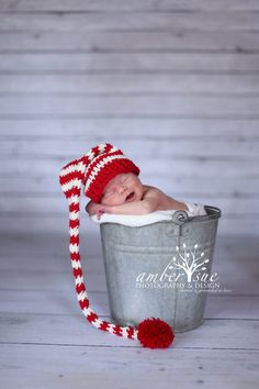 a newborn baby in a bucket wearing a red and white knitted hat with pom - poms