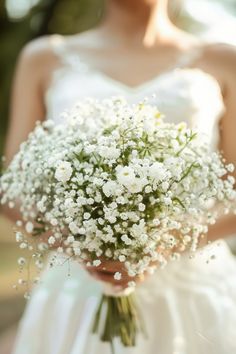 a woman in a wedding dress holding a bouquet of white baby's breath flowers