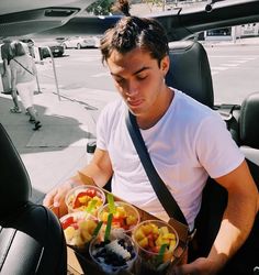 a man sitting in the back seat of a car holding a box of fruit and salads