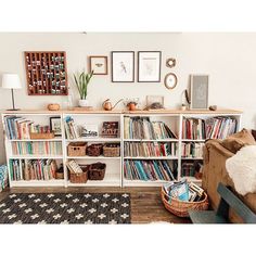 a living room filled with lots of books on top of a white book shelf next to a couch