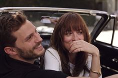 a man and woman sitting next to each other in front of a car