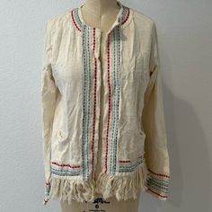 A Cream-Colored, Long-Sleeved Garment, Likely A Jacket Or Cardigan; The Garment Features Intricate Embroidery Of Colorful Flowers And Butterflies Across The Upper Back. The Lower Hem Is Adorned With Fringe And Decorative Stitching In Red And Blue. The Fabric Is Lightweight And Textured, Contributing To A Casual, Bohemian Aesthetic. Embroidered Outerwear For Daywear In Fall, Embroidered Outerwear For Fall Daywear, Embroidered Fall Outerwear For Daywear, Beige Embroidered Cotton Cardigan, Traditional Long Sleeve Spring Cardigan, Beige Embroidered Bohemian Cardigan, Bohemian Beige Embroidered Cardigan, Beige Bohemian Embroidered Cardigan, Bohemian Cotton Cardigan For Daywear