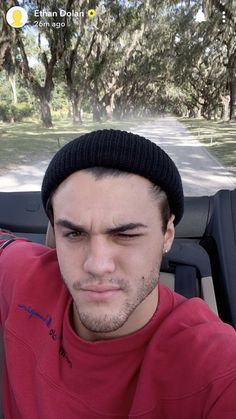 a man in a red shirt and black beanie driving down a road with trees behind him