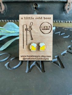 a pair of yellow glass earrings on top of a wooden plaque with the words little gold bee