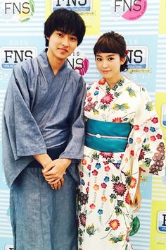 two people standing next to each other in front of a blue and white wall with flowers on it