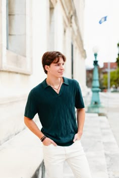 a young man standing on the side of a building with his hands in his pockets