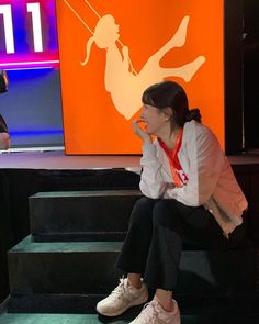 a woman sitting on some steps in front of a tv screen with an orange sign behind her