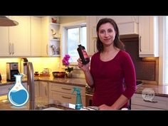 a woman standing in a kitchen next to a sink and counter top with a bottle on it