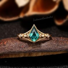 a gold ring with an emerald colored stone in the center on top of a piece of wood