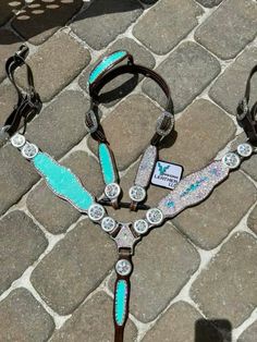 two horse bridles with turquoise and white designs on them sitting on the ground