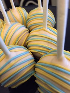 several yellow and blue striped cake pops on a black table with white sticks sticking out of them