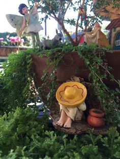 a yellow hat sitting on top of a tree stump next to plants and figurines