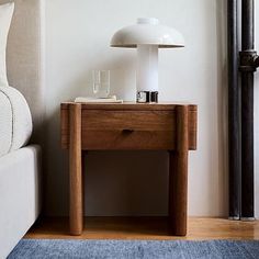 a white lamp sitting on top of a wooden table next to a bed in a bedroom