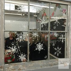 two women standing in front of a window decorated with snowflakes