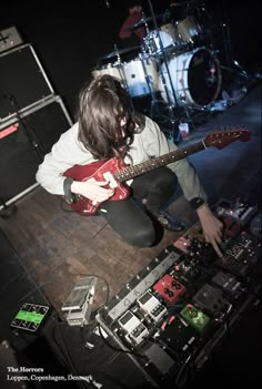 a person sitting on the floor with a guitar in front of him and other musical equipment behind them