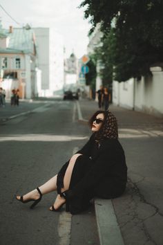 a woman sitting on the side of a road with her legs crossed and wearing sunglasses