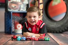 a young boy sitting on the floor with toy cars in front of him and smiling