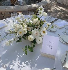 the table is set with white flowers and place cards for guests to sit down at