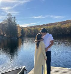 a man and woman standing on a dock next to a body of water with trees in the background