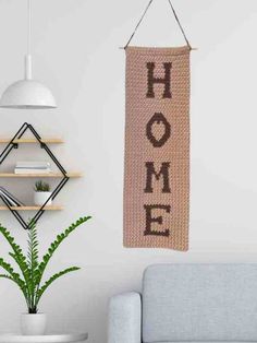 a wall hanging with the word home on it next to a couch and potted plant