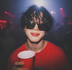 a person with sunglasses holding a cup in front of their face at a nightclub or club