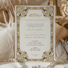 an ornate wedding card with pearls and feathers on the table next to some other items