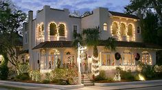 a large white house with christmas lights on the windows and trees in front of it