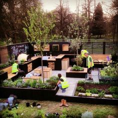 two people in yellow vests are working in a garden with raised beds and benches