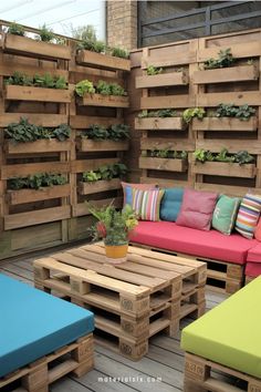 Outdoor seating area with colorful cushions and wooden pallet furniture, surrounded by vertical pallet planters filled with various green plants.