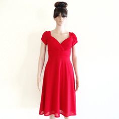 a mannequin dressed in a red dress stands against a white wall