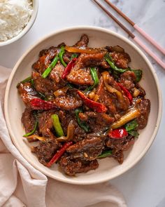 a white bowl filled with meat and vegetables next to rice on top of a table