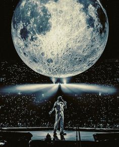 an astronaut standing on stage in front of the moon with his hands up to his chest