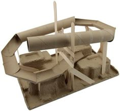 a cardboard model of a boat with sand on the bottom and two poles sticking out of it