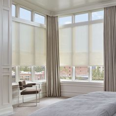 a bed sitting under two windows in a bedroom next to a window with drapes