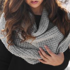 a woman wearing a gray and white knitted scarf with her hands on her chest