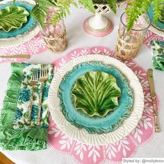 the table is set with plates, silverware and green plants