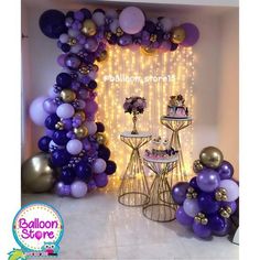 purple and gold balloons are on display in front of a cake table with two small tables