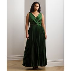 a woman in a long green dress stands against a wall and looks off to the side