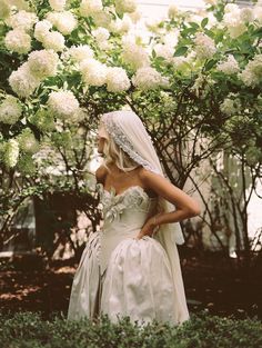 a woman in a wedding dress standing under a tree with white flowers on the branches