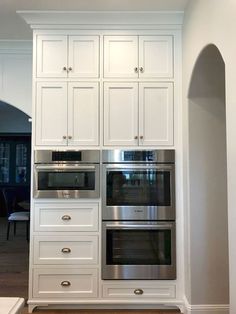 a kitchen with white cabinets and stainless steel ovens in the center, along with an arched doorway