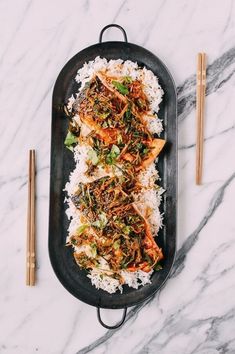 a black plate topped with rice covered in meat and veggies next to chopsticks